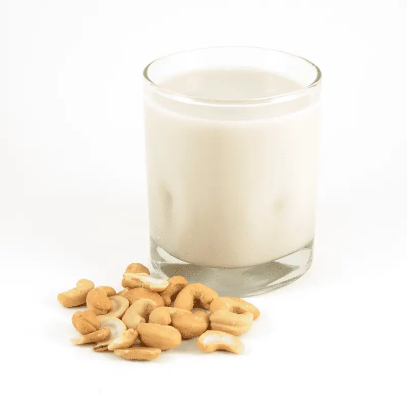 A cold glass of cashew milk next to a pile of cashews isolated on a white background.