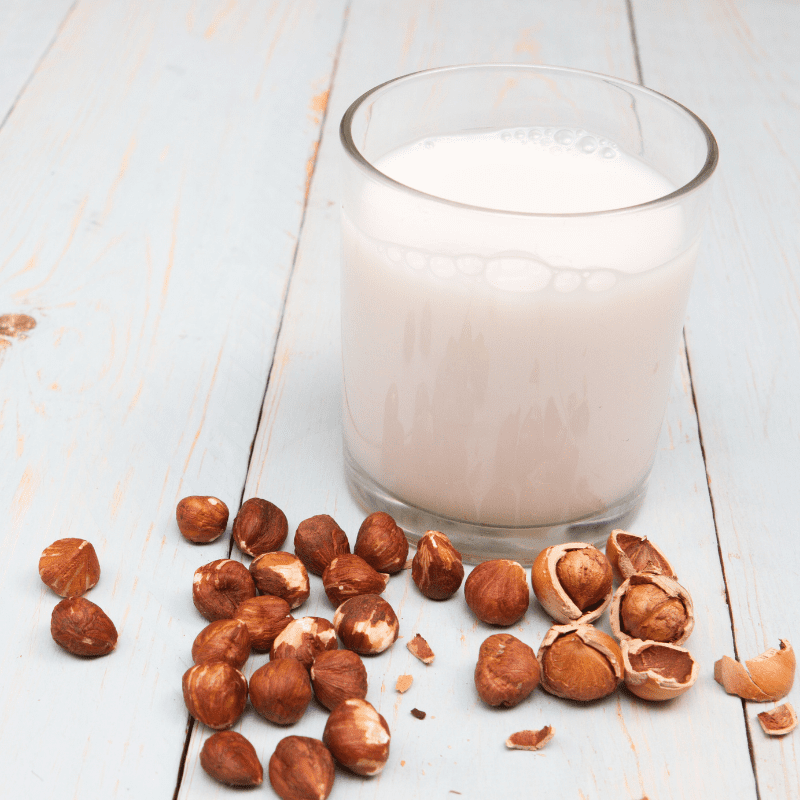 A glass of hazelnut milk with hazelnuts on a wooden table - vegan milk