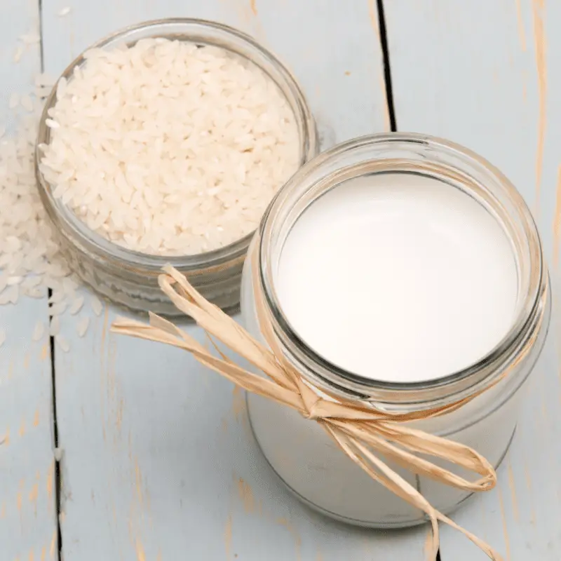 A glass of rice milk with rice grains on a wooden table - vegan milk