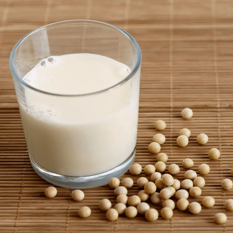 Glass of soya milk with froth on bamboo mat with spilled soya beans.