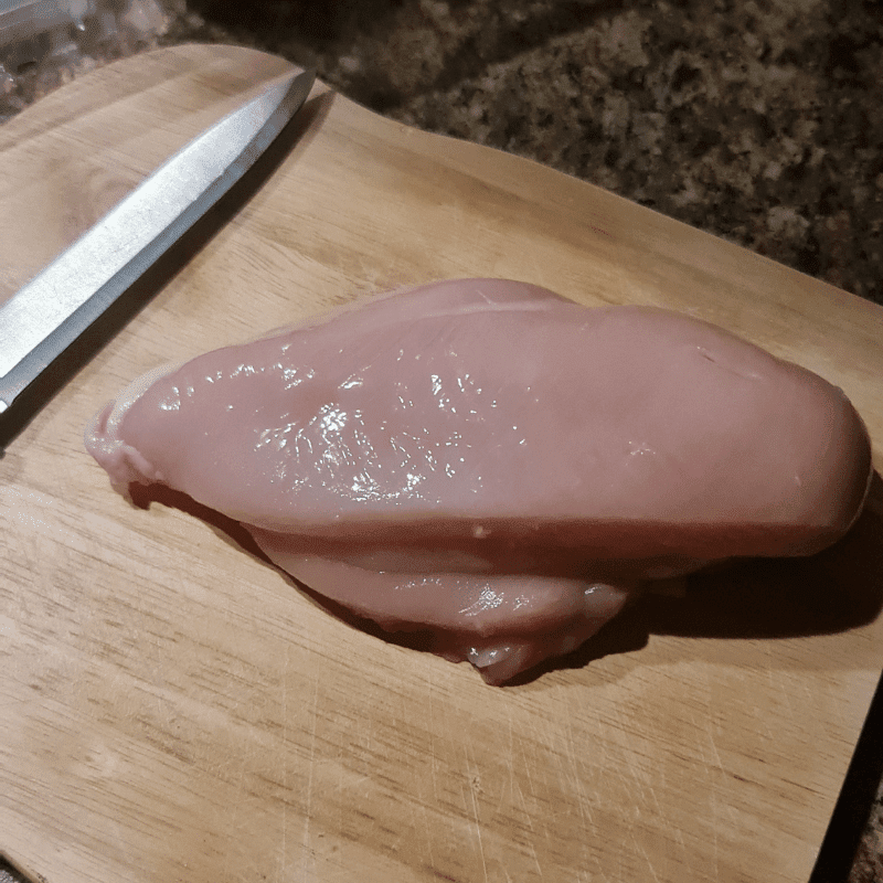 A raw chicken breast, knife and chopping board