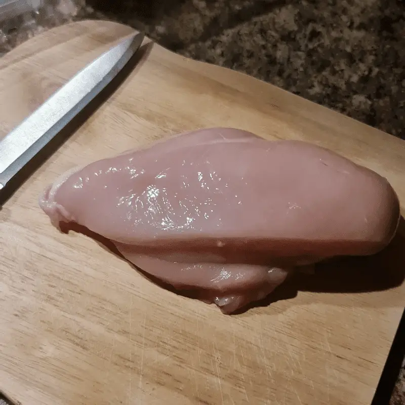 A raw chicken breast, knife and chopping board