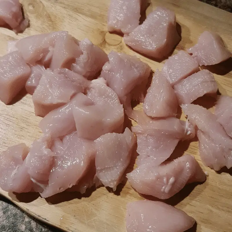Chunks of raw chopped up chicken chunks on chopping board